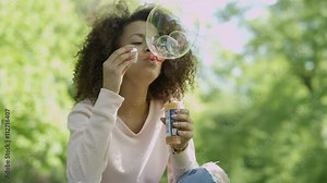 Beautiful woman blowing bubbles in sunny park. Outdoor summer portrait of young beautiful happy woman making soap bubbles. Joyous happy girl in park.