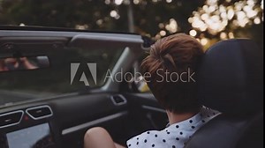 Woman enjoying ride in a convertible car on summer sunset. Cinematic view of happy unrecognizable young elegant dancing woman in a passenger seat of a convertible. Freedom and happiness of vacation. Stock Video