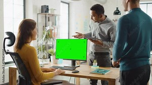 Three Start-up Entrepreneurs Work on Desktop Computer with Green Mock-up Screen, They Discuss Project Design, Use Touch Screen Digital Tablet. Modern Stylish Office with Diverse Team of Professionals
