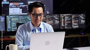 Asian Male Programmer Having A Meeting By A Laptop While Writing Code On Multiple Monitors Showing Database On Terminal Window Desktops In The Office
