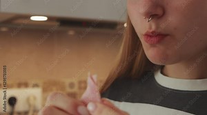 Young woman enjoying ham slice, nose piercing visible, standing in modern kitchen with relaxed culinary contentment