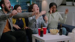 Mixed race people cheering together while looking at soccer on television. Multiethnic friends celebrating goal team enjoying match championship while sitting on sofa late at night in living room