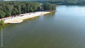 tilt aerial footage of a sandy beach along the banks of Lake Acworth with rippling green waters and people in the water and relaxing on the beach with umbrellas in Acworth Georgia USA
