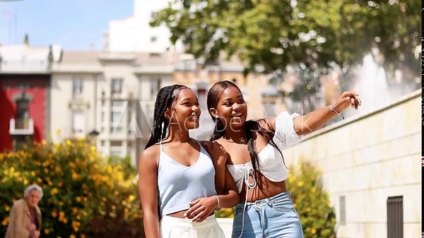Video of two Hispanic young women walking down the street, talking and laughing and then pointing excitedly, front view in motion