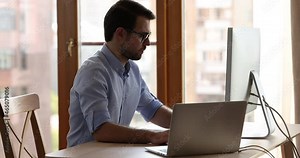 Sync data. Young man work at home office connect two computers within single network share information in domestic device group. Skilled male user sit at desk transmit files from desktop to laptop pc