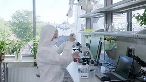 Scientists in protection suits and masks working in research lab using laboratory equipment: microscopes, test tubes. Biological hazard, pharmaceutical discovery, bacteriology and virology.