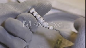 Dental technician polishing artificial ceramic teeth using sandblaster in the dental lab. Professional wearing gloves while holding fake teeth in hand and polishing it with sand blaster.