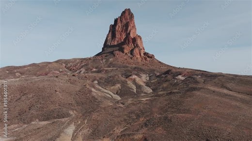 Aerial drone footage of Agathla Peak, also known locally as El Capitan, in northern Arizona. Smooth upward reveal showing the volcanic rock formation rising from the desert near Monument Valley.