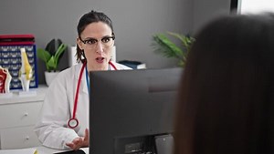 Two women doctor and patient using touchpad having consultation at clinic