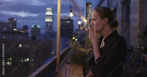Attractive young woman smokes a cigarette in front of the night skyline from a balcony in Downtown Los Angeles, California. Recorded in slow motion at 60fps.