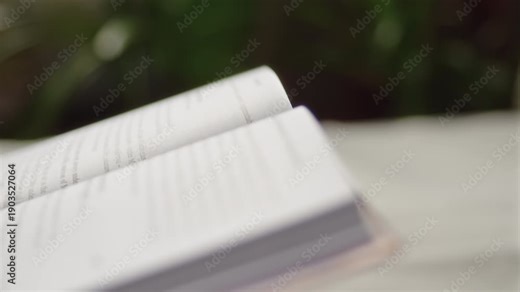 Close-up, a woman's hand turning a page of a book while reading while sitting at a table