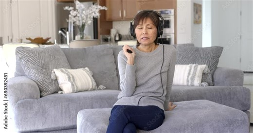 Beautiful woman wearing headphones looking at camera enjoying using remote control changing television channels
