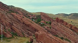 Drone aerial tracking right over layered sandstone ridges at Red Rocks Amphitheatre with sweeping view of Colorado foothills