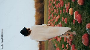 A stylish girl walks in a field with pumpkins. A woman walks forward among the pumpkins. Rear view. Agricultural lands. Farming. Harvesting. Thanksgiving vegetable display. Vertical video.