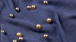 Large multi-colored pearl beads fall on blue cotton fabric, textile background, slow motion
