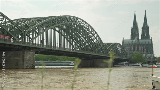View of cologne cathedral and Hohenzollern Bridge from right side and ships on Rhine river slow motion. Famous Cologne Bridge and moving clouds in the sky: Germany, Cologne - 20 May 2024