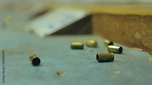 Empty pistol bullet shells dropping and impacting wooden table in a shooting range. Extreme close up, selective focus with blur background and copy space.
