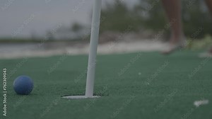 Person putting orange golf ball into hole - low, close up shot