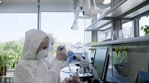 Scientists in protection suits and masks working in research lab using laboratory equipment: microscopes, test tubes. Biological hazard, pharmaceutical discovery, bacteriology and virology.