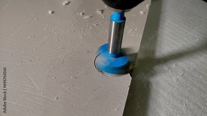 A craftsman drills a Forstner bit hole for furniture hinges in a wooden slab