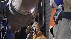 A welder engaged in industrial metalwork focuses on joining large pipes with a high-intensity welding torch, showcasing precision and skill critical to metal fabrication and construction.