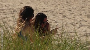 Two women are relaxing and sunbathing on the beach, lying on the warm sand. The scene captures a peaceful moment of leisure and enjoyment under the sun.
