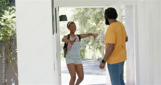 Father holding door open greeting teenage daughter entering at home, lifting phone and hugging