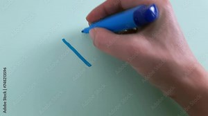 YES. Woman's hand writes the word Yes with blue marker on light blue paper background.