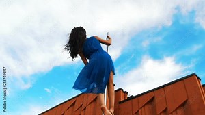 Young woman in blue dress dancing pole-dance outdoors