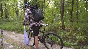 Volunteer bicyclist remove trash bags for garbage, clean up forest during bicycle ride. Save environment. Recycle waste litter rubbish garbage trash junk clean training. Picking up trash while cycling