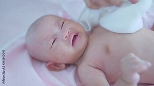 Baby girl crying after bath in a pink towel and hand of mother.
