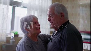 Happy senior couple dancing together at home by kitchen window. Joyful caucasian elderly husband and wife smiling while holding hands in dance