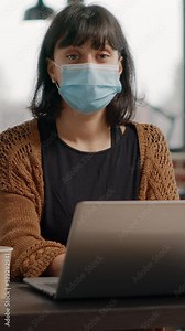 Portrait of employee with face mask using laptop to work on business strategy and project planning in startup office. Woman working with technology for development during pandemic.