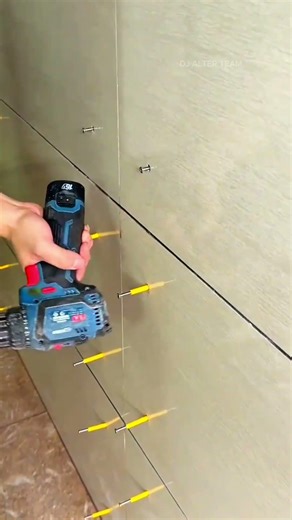 Installing wall tiles using a cordless drill to adjust leveling spacers for even grout spacing