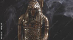 golden statue of the Egyptian god Ra in smoke on a black background