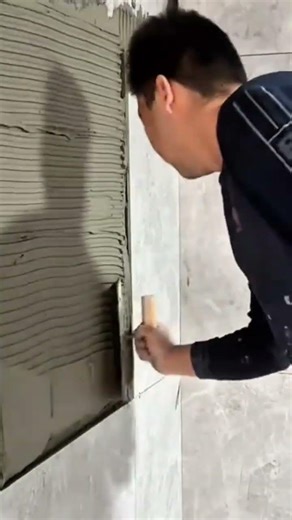 applying adhesive to concrete wall then positioning and pressing large grey tiles into place firmly