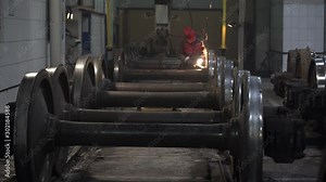 Repair of axles of rail vehicles. Many axles of rail vehicles in the repair shop. Worker inspects and polishes steel wheels.