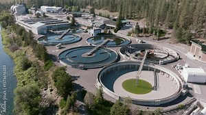 Multiple circular clarifier tanks sit beside the river in a visually striking arrangement, highlighting the industrial design and layout of the facility.