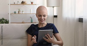 Bald girl sit on couch in living room use tablet start finish videocall conversation. Oncology nurse practitioner provide help by online video conference. Cancer patient of E-medicine client concept