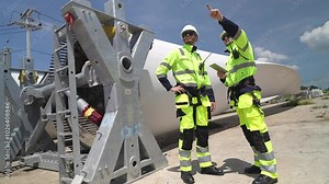 engineers in high visibility safety gear conduct a detailed inspection of a wind turbine blade at a construction site. The massive blade lays on the ground, highlighting renewable energy technology. Stock Video