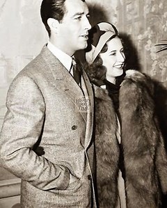 "Barbara Stanwyck marries her second husband, actor Robert Taylor, in an elegant San Diego ceremony in 1939. The celebrated Hollywood couple, both at the height of their careers, exchange vows surrounded by close friends and family. Stanwyck, radiant in a classic bridal gown, and Taylor, dashing in formal attire, embody the glamour and sophistication of 1930s Tinseltown. Photographers capture their joyous expressions as they celebrate the beginning of their life together. The union of two cinema