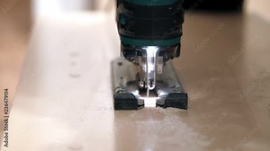 Work with a manual electric fret saw. Making a direct cut in a wooden plate. Visible small wooden shaving.