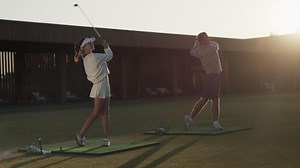 Partners swing golf clubs sending balls to goals at sports center