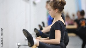 Little girls in black leotard are stretching at the ballet class.