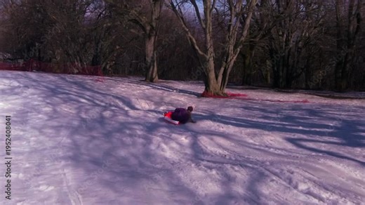 A high-speed action shot of a child sliding down a snowy hill using a plastic bag as a sled. A creative and sustainable way to reuse old materials for winter fun in 2026. Keywords: sledding, snow, win