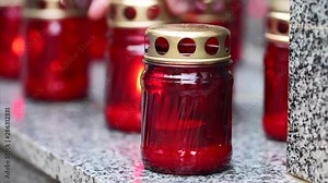 Memory candles in red jars. Lights grave candle with lighter for fallen people, soldiers and victims on monument memorial steps, closeup view.