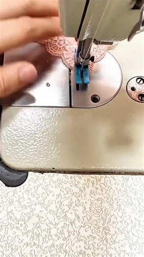 sewing the pink lace fabric carefully using a silver industrial sewing machine