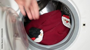 Santa Claus putting into the washing machine red hat, socks and Christmas-tree set, Preparation to Christmas and New year holidays, Christmas humor, prank and fun