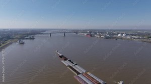 Wide aerial footage of a couple of tugboats pushing a large amount of barges on the Mississippi River in Baton Rouge, Louisiana.