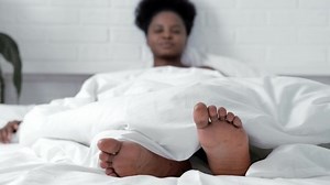Lazy morning, Young black girl in pajamas stretching in her bed, napping at home in bedroom, legs close up.